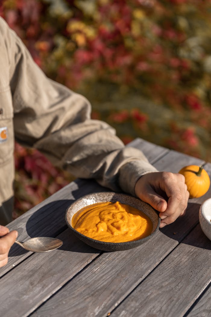 Close-up of creamy pumpkin soup with spoon, perfect for fall dining outdoors.